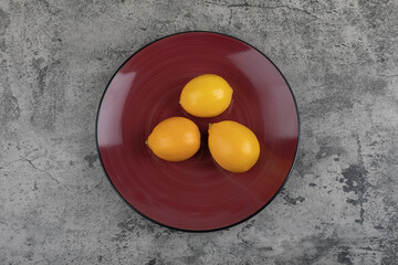 Burgundy plate and fresh juicy lemons on stone background