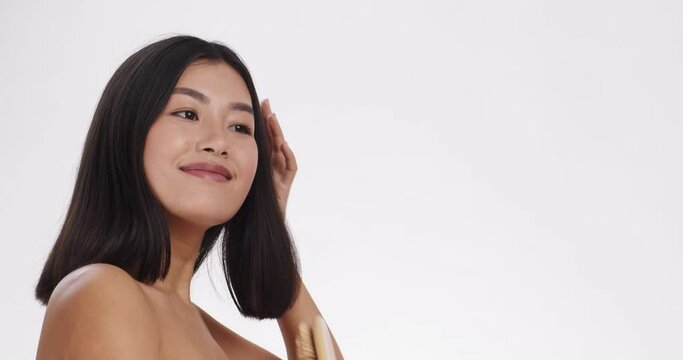 Young pretty asian woman brushing her hair with massage hairbrush and smiling, white background with empty space