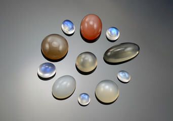 Set of natural moonstone cabochones. Round, oval shaped gems. Blue radiance glow adularia, yellowish gray color, salmon light peech and milky gray with light cat's eye effect. Gray radial background.