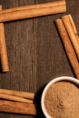 Finely ground cinnamon in a white ceramic bowl. Cinnamon sticks on a dark background with negative space to place logo or text.