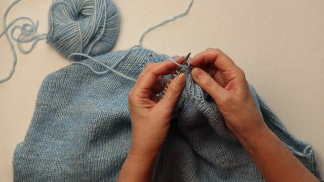hands knitting a sweater of blue wool yarn with knitting needles