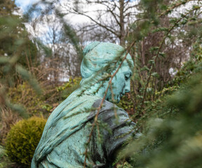 Statue mit viel Patina hinter Büschen 