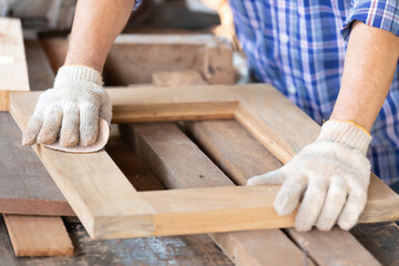 closeup man carpenter using sandpaper on a piece of wood in workshop