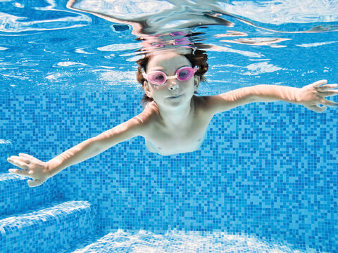 Little child swims underwater in swimming pool, happy active girl dives and has fun under water, kid fitness and sport 
