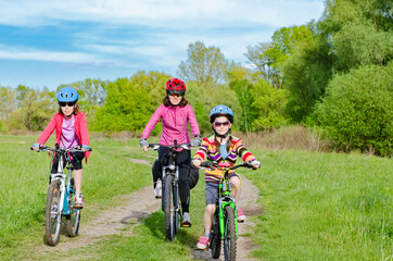 Fototapeta na wymiar Happy mother and kids on bikes cycling outdoors in park, active family sport and fitness together 