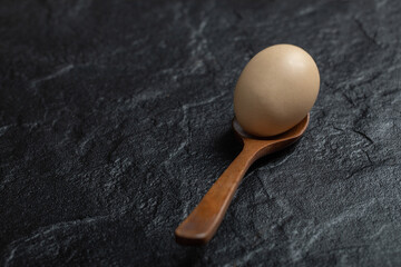 Wooden spoon of organic raw egg on black background