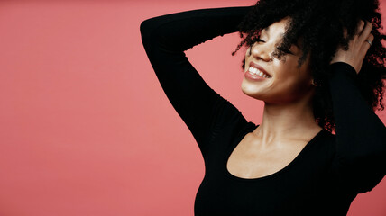 joy dances her hands near her hair and looks into the camera portrait of a young Afro-ethno woman. A model in a photo studio poses on a scarlet background.