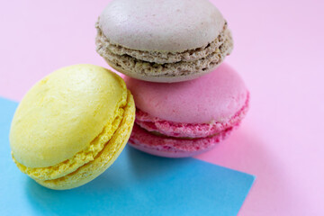 Three macaroons french pastry. Brown, pink and yellow almond cookies on two colored background