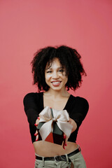 Shows holding a black gift box with a bow. young woman of Afro appearance, curly lush hair. She is dressed in a black comfortable jacket. He looks at the camera and smiles. Copy space.