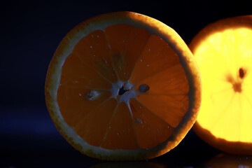 Composition with orange and grapefruit slices on a black background. A slice of orange with back light on a black background with water drops. Juicy orange on a table.