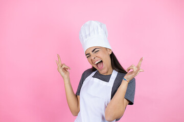 Young hispanic woman wearing baker uniform over pink background smiling, feeling carefree, relaxed and happy, dancing and listening to music, having fun at party
