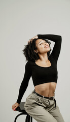 positive playful sweet young beautiful confident woman of African appearance ethnics. sitting on a chair in a photo studio, curly brunette black hair. the manager is a freelance student.