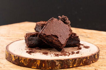Pieces of fresh chocolate brownie on wooden plate on white background. Stack of fudgy chocolate brownies on white background, homemade bakery and dessert. Brownie chewy squares stack on wooden plate.