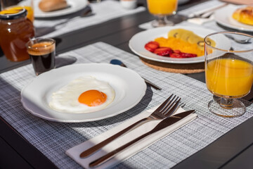 Breakfast is served on top of a table, with an egg on a plate, fruit, orange juice, coffee. Close up shot.