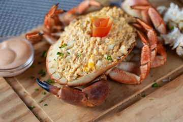 Closeup of a crab shell filled with a mixture of egg, mayonnaise and crab meat on a wooden board.