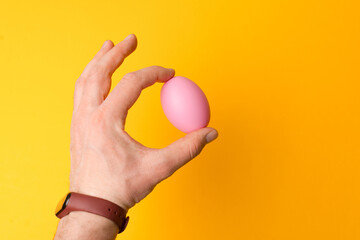 Close up photo of male hand holding pink easter egg.