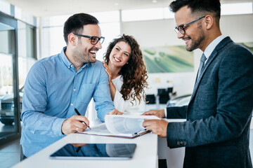 Middle age couple choosing and buying car at car showroom. Car salesman helps them to make right decision. Man signs buyers contract.
