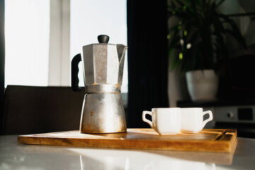 Hot, aromatic Americano coffee. Geyser coffee maker made of aluminum metal. two white mugs for coffee Americano espresso. It's on the table.Sunlight from the window.