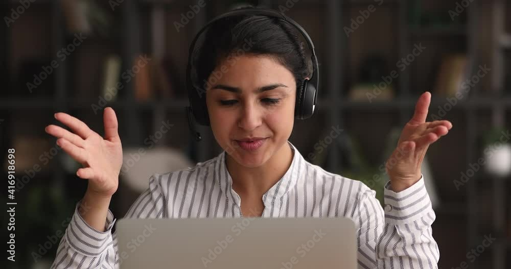 Canvas Prints Friendly smiling millennial indian businesswoman in wireless headphones with microphone waving hand making hello gesture, starting online meeting web camera video call conversation with colleagues.