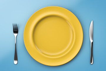 Empty bright yellow plate on a blue table. Fork and spoon. Healthy nutrition topics.