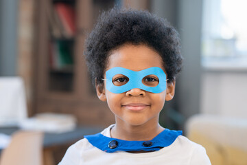 Cute boy in costume of superhero looking at you through blue paper eyeglasses