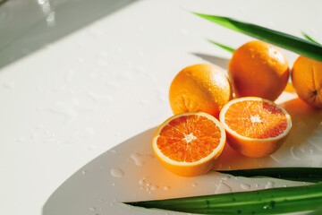 Healthy food. Healthy lifestyle. Red oranges. Real live vitamin C. They are lying on a white table. Long green leaves from a palm tree. Fresh delicious fruits. copy space.