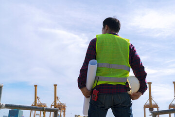 Engineer man wearing safety helmet and hold blueprints at a cargo port facility