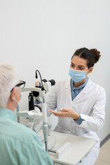 Young female ophthalmologist going to test eyesight of senior male patient