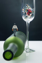 miniature people. man addicted to alcohol is walking on a bottle against the background of a glass with ruined lives. the problem of alcoholism in society