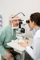 Young brunette ophthalmologist in whitecoat testing eyesight of senior man