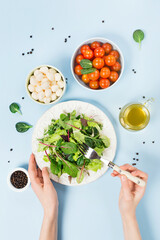 Healthy green salad on white plate with fresh salad leaves, tomatoes and mozzarella cheese on blue background