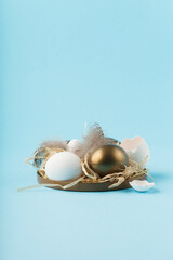 Easter white golden eggs, quail eggs and feathers on blue background.