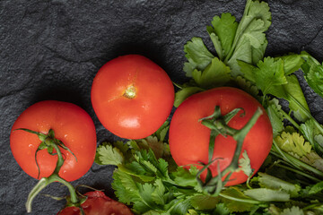 Close up photo of fresh ripe tomatoes and coriander leaves on black background