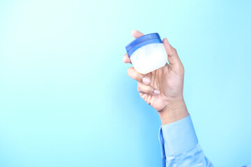 hand holding petroleum jelly against blue background 