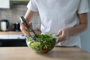 Close up of woman cooking vegetable salad at home kitchen. Female hands stirs vegetarian salad of fresh herbs and bell pepper, cherry tomatoes. Slimming diet. 