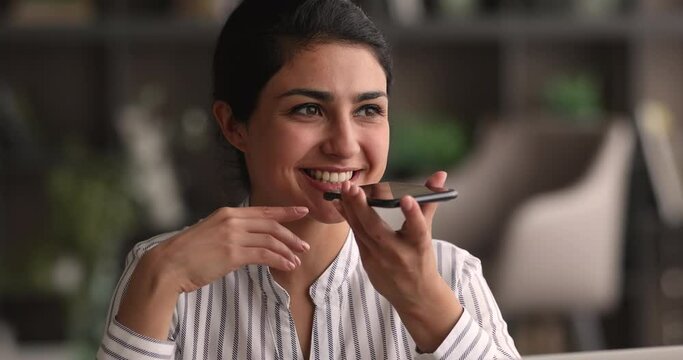 Head shot sincere happy millennial attractive mixed race indian woman recording audio message, holding loudspeaker conversation, responding on voicemail, enjoying distant communication online.