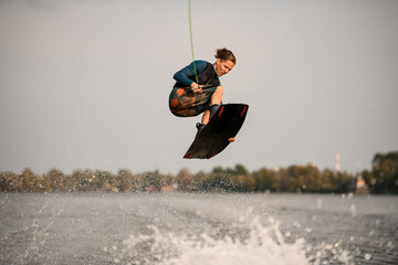 young energetic wakeboarder jumping high over river water