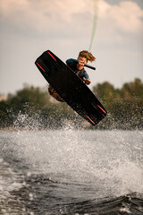 young man on wakeboard vigorously jumps and performs tricks over the water.