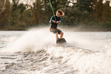 Beautiful view of man holding bright cable and balancing on wakeboard on wave.