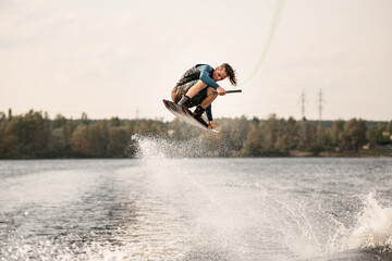 athletic man with bent knees jumps on wakeboard over the water