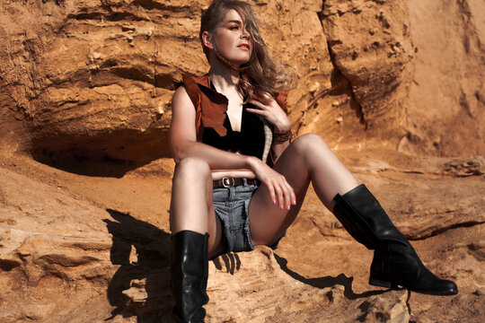 Beautiful woman dressed cowboy style clothes posing with lizard against the camel background. Bearded agam the home pet of girl walking in the nature with owner