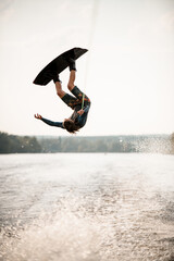 Young athletic man having fun on wakeboard masterfully jumps over splashing river water