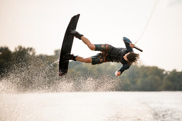 active male wakeboarder doing somersault in the air above water