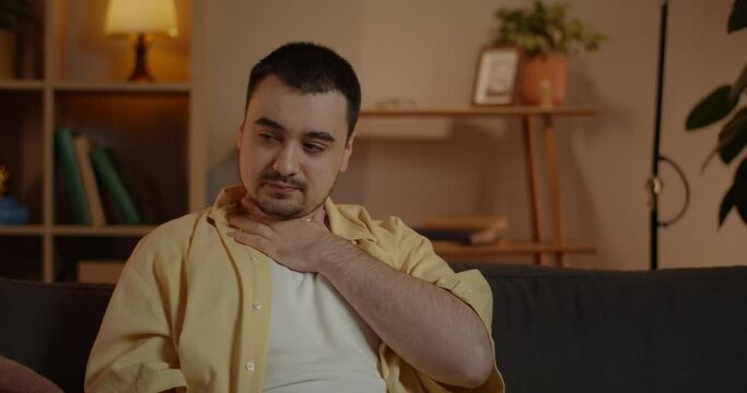 Crop guy looking bad and caughing. Caucasian male person feeling ill and having sore throat while sitting on sofa at home.Concept of people health, illness, viruses.