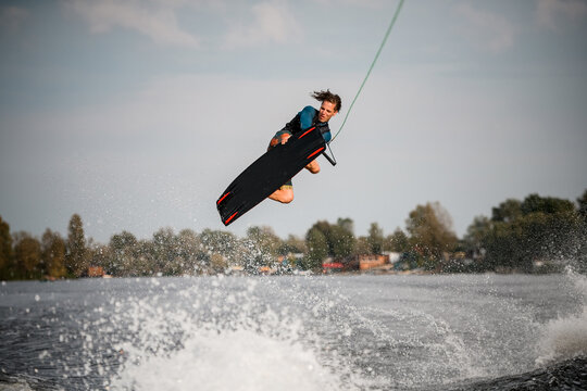 young man on wakeboard spectacularly jumps and performs tricks over the water. - Powered by Adobe