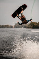 sportive guy doing extreme high jump on wakeboard over splashing river wave
