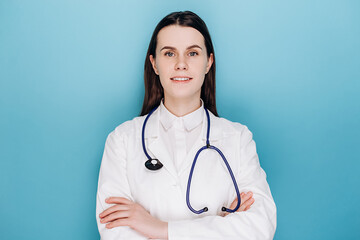 Portrait of cheerful kind brunette young woman consultant apothecary qualified expert medicare help assistance, cross arms chest, isolated on blue studio background. Doctor ready for shift in clinic