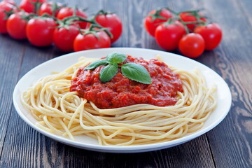 Spaghetti, pasta with tomato sauce and fresh cherry tomatoes on rustic wooden table.