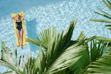 Enjoying suntan. Tropical vacation concept. Top view of young woman on the yellow air mattress in...