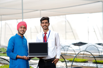 Fototapeta premium Young indian farmer and agronomist laptop screen at greenhouse